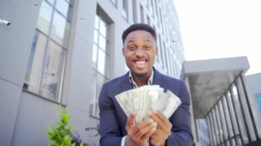 Mutlu Afrikalı Amerikalı iş adamı sayımı, dalgaları, atışları, gösterişi, gösterişi, nakit para arka planı kameraya bakan modern bir ofis binası. Kazananı borsa bahislerinde kutlayın.