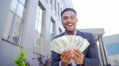 Mutlu Afrikalı Amerikalı iş adamı sayımı, dalgaları, atışları, gösterişi, gösterişi, nakit para arka planı kameraya bakan modern bir ofis binası. Kazananı borsa bahislerinde kutlayın.