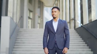 Genç özgüvenli Afro-Amerikan iş adamının modern ofis binasının arka planında duran ciddi iş adamına baktığı portre. Erkek, kollarını kavuşturmuş resmi bir takım elbise.