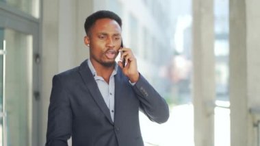 Afrika kökenli Amerikalı erkek işadamı dışarıda cep telefonuyla konuşuyor. İş adamı dışarıyı arıyor. Akıllı telefondan sinirli, profesyonel bir konuşma. Şehir caddesinde sinir bozucu bir konuşma