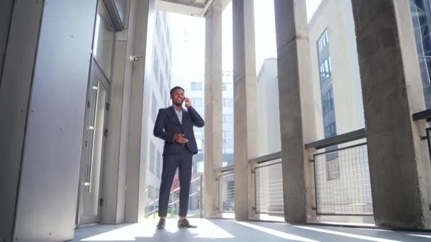 ポートレート成功した若い従業員自信を持ってアフリカ系アメリカ人ビジネスマンの背景を話す現代的なオフィスビルディングビジネスマンの会話携帯電話立って正式なスーツ屋外都市通り — ストック動画