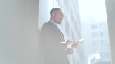 Resmi takım elbiseli genç Afro-Amerikan iş adamı dışarıda arka plandaki modern ofis binasında elinde tabletle çalışıyor. Şehir dışında akıllı telefon ya da cep telefonu kullanan bir adam.