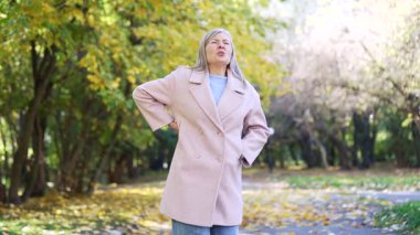 Yaşlı kadın dışarıda akut sırt ağrısı çekiyor. Yaşlı, olgun bir kadın, bel ağrısından muzdarip bir şekilde omurga tutuyor. Dışarıdaki caddede acı verici bir duruş sergiliyor.