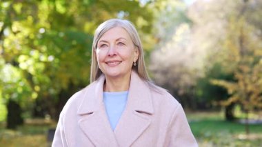 Parkta yürüyen zarif, mutlu, kıdemli bir kadın, açık havada gülümseyen yaşlı, yaşlı, güzel, ceketli bir bayan, doğanın tadını çıkarıyor, sağlıklı bir yaşam tarzı güzellik, yaşlanan temiz hava, sonbahar uykusu, yakın dinlenme.