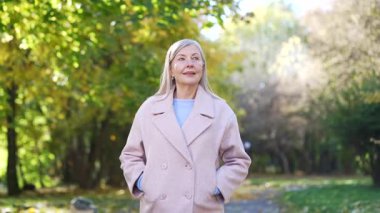 Mutlu yaşlı, kır saçlı, parkta yürüyen, gülümseyen yaşlı, ceketli yaşlı bir bayan, doğanın tadını çıkaran, sağlıklı yaşam tarzı güzelliği, zarif bir şekilde yaşlanan temiz hava, sonbahar uykusu.