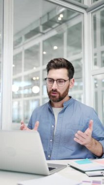 Kendine güvenen iş adamı iş yerindeki bir dizüstü bilgisayarla video görüşmesinde konuşuyor. Girişimcinin bir iş toplantısı var. Müdür çevrimiçi bir konferansta uzaktan konuşuyor. Dikey