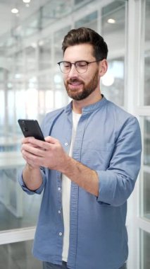 İşadamı, modern bir iş ofisindeki iş yerinde cep telefonunu kullanıyor. İşçi internette sohbet ediyor, başvuruda çalışıyor ya da akıllı telefondan mesaj okuyor. Dikey video