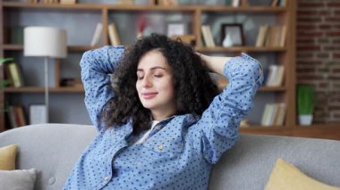 Genç bir kadın, gözleri kapalı ve elleri başının arkasında evdeki bir kanepede otururken rahatlıyor. Sakin, mutlu, güzel bir kadın derin derin nefes alıyor, huzuru hissediyor. Kapat.