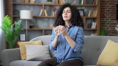 Alerjik kadın hapşırır ve burnunu mendille siler. Evdeki oturma odasındaki kanepede oturan, mevsimsel alerjiden muzdarip sağlıksız genç bir kadın. Kız soğuk algınlığı, virüs ya da grip olmuş.