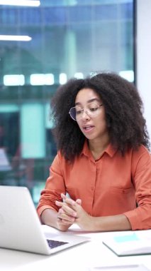 Kendine güvenen Afro-Amerikan iş kadını ofiste dizüstü bilgisayarla konuşuyor. Kadın yönetici online bir konferansta iletişim kurar ya da iş ortağıyla uzaktan sohbet eder. Dikey