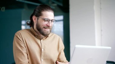 Gülümseyen iş adamı, modern iş ofisindeki iş yerinde otururken bilgisayar kullanarak video konferansında konuşuyor. Koç ya da öğretmen çevrimiçi eğitim, danışmanlık, kurs ya da webinar alıyor. Kapat.