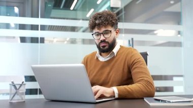 Hayal kırıklığına uğramış işadamı, modern iş ofisindeki iş yerinde otururken dizüstü bilgisayarından kötü haberler okuyor. Endişeli erkek işçi, bilgisayardaki olumsuz mesaj bilgilerini incelerken üzülüyor