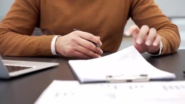 İş yerindeki bir masada bir işadamının el imzalı belgelerini kapatıyoruz. Günlük süveter giyen bir yönetici ya da yönetici belgeleri inceler ve sözleşmeyi kalemle imzalar.