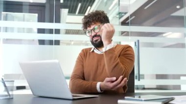 İş yerinde masa başında çalışırken dirsek ağrısı çeken bir iş adamı. Sağlıksız erkek bir eklem masajı yapıyor, eliyle hassas bir noktayı tutuyor. Eklem yaralanması ya da bağ burkulması var.