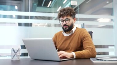 Memnun iş adamı, modern cam iş ofisindeki çalışma masasında otururken dizüstü bilgisayarından harika haberler aldı. Gülümseyen erkek profesyonelin bilgisayardan olumlu mesaj okumasına sevindim.