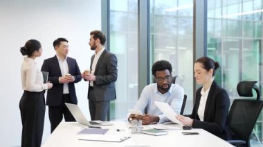 İki iş arkadaşı, kadın ve erkek iş yerindeki çeşitli işçilerin çalışma masasında otururken ellerinde belgelerle konuşuyorlar. Takım çalışması ve işbirliği. Dostça pozitif işbirliği