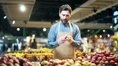 Süpermarkette ya da markette çalışan yakışıklı bir manav ya da küçük bir işletme sahibi tezgahın arkasında çalışan meyve reyonunun yanındaki elma topluyor.