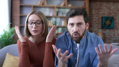 Webcam görüntüsü. Üzgün evli çift, aile psikoloğu ile video görüşmesinde konuşurken evdeki kanepede oturup kameraya bakıyor. Üzgün adam ve kadın, aile sorunları hakkında psikoterapiste şikayette bulunuyor.