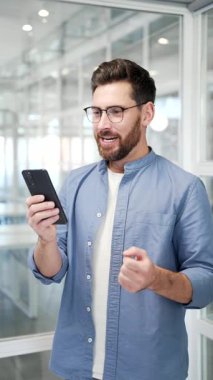 Mutlu iş adamı iş yerindeki cep telefonundan harika haberler aldı. Gülümseyen şaşkın girişimci olumlu bir mesaj okuyarak başarıyı kutluyor. Dikey video