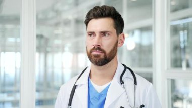 Modern hastane kliniğinde kameraya bakan beyaz önlüklü ciddi bir doktorun portresi. Ofis ortamında poz veren kendine güvenen profesyonel doktor. Kapat.