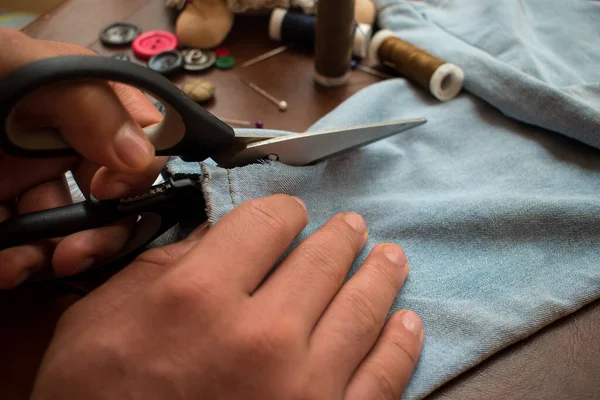 Tailor using some scissors cutting some pants on a table