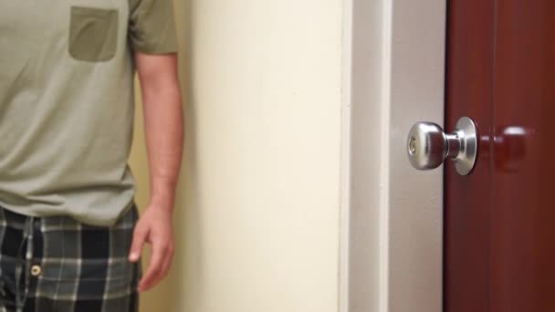 家で木製のドアを開ける再生パジャマと緑のTシャツを着て若い男 — ストック動画