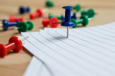 Metal ataçlar ve ahşap bir masanın üzerinde bazı çarşaflarla renkli raptiyeler. 