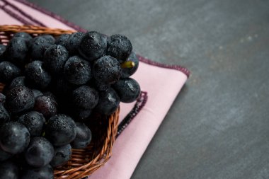 Üzerinde pembe masa örtüsü olan siyah bir sepetin içindeki üzümler. 