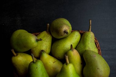 Siyah ahşap bir masada sepetin içinde taze ve yeşil armutlar. 