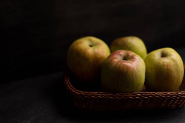 Siyah ahşap bir masada kırmızı elmalı bir sepet.  