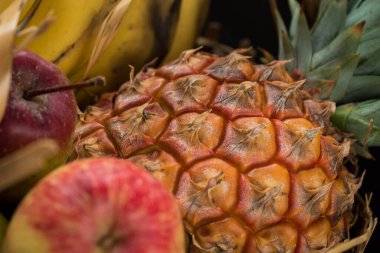 Biraz muz, elma ve siyah arka planı olan siyah bir masada sepetin içinde bir ananas. 