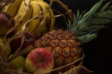 Biraz muz, elma ve siyah arka planı olan siyah bir masada sepetin içinde bir ananas. 
