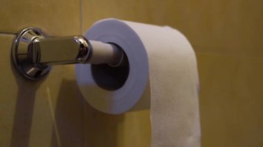 Yeni kağıt rulo sarı arka planı olan bir banyoda bazı eller tarafından kesiliyor. 