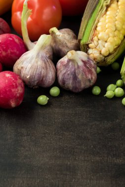 Mısır, domates, havuç, patates, patlıcan, turp ve diğer sebzeler siyah ahşap bir masada. 