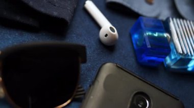 Mavi bir masadan güneş gözlüğü ve siyah bir cep telefonuyla beyaz kablosuz bir kulaklık alıyorum.