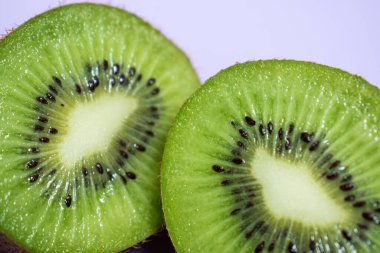 Parlak mor bir yüzeye iki taze kesilmiş kivi parçası yakın çekim