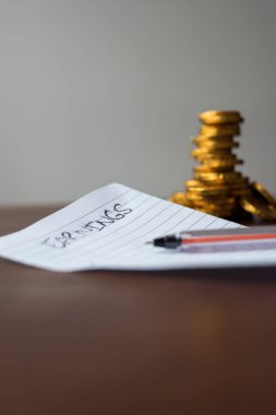 Kâr listesi olan altın sikkeler ve ahşap bir masada siyah bir kalem.