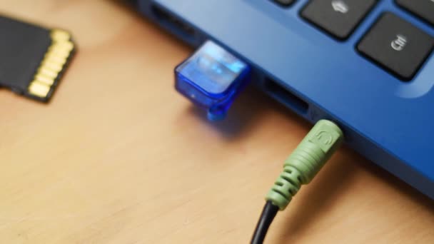 耳机电缆连接在木制桌子上的蓝色现代笔记本电脑 Usb存储器和Sd存储器上 — 图库视频影像