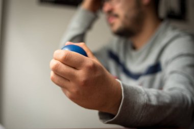 Gözlüklü stresli adam, küçük mavi stres topunu sıkıyor ve kafasını kaşıyordu.