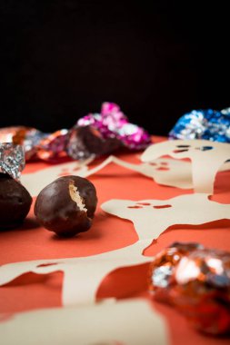 Bazı çikolatalar, farklı renkte ambalajlar ve turuncu yüzeyde kağıt hayaletler. 