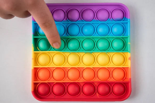 Beyaz bir masada, renkli bir çocuk oyuncağını iten parmak. 