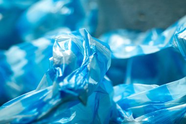 Tek kullanımlık plastik atık, kirlilik ve çevresel etkiyi temsil eden parlak doku ve kıvrımları gösteren buruşuk mavi plastik poşetlerin yakın çekimi.