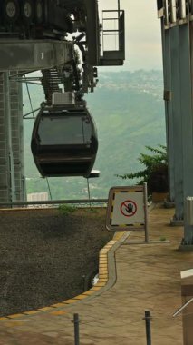 Kablolu araba yolculuğuna başlıyor, yeşil yemyeşil tepeler ve arka plandaki uzak binalar, hava taşımacılığı kavramları için zeminde uyarı işareti.