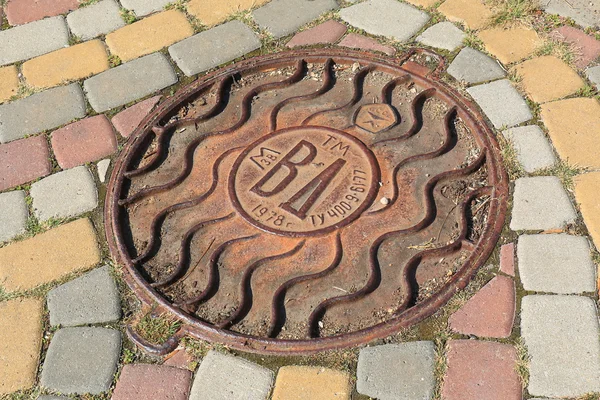 Rusted manhole on a street with pavement from multicolor block — Stock Photo, Image