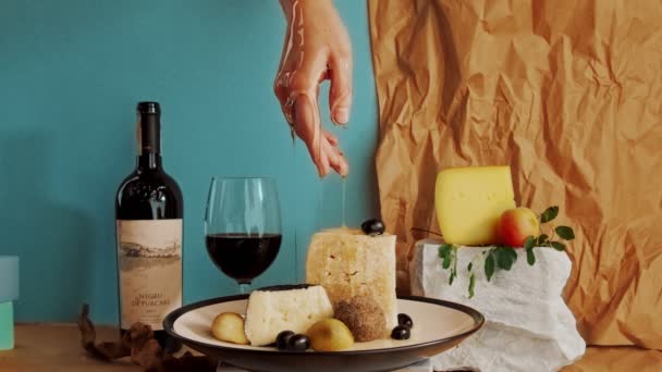Composición de varios tipos de queso y una botella de vino se complementó con una mano femenina frágil de la que gotea bellamente miel — Vídeos de Stock