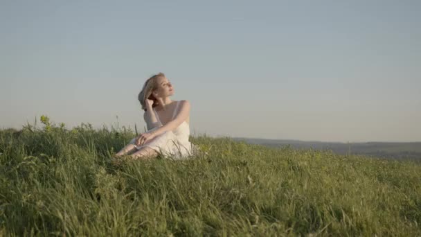 Молодая девушка в белом платье наслаждается жизнью на лугу — стоковое видео