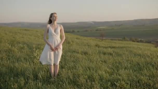 Nieśmiała dziewczyna w białej sukience jest zachwycona prądami powietrznymi na łące — Wideo stockowe