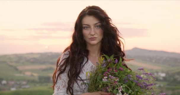 Девушка в горах с цветами в руках на закате — стоковое видео