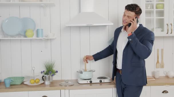 Jeune homme d'affaires attrayant parle sérieusement au téléphone et mélange des repas préparés — Video