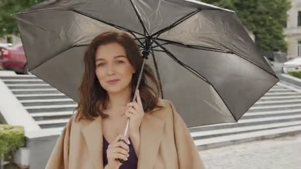 Una atractiva mujer retira suavemente su campo de la cámara y se esconde detrás de un paraguas — Vídeos de Stock